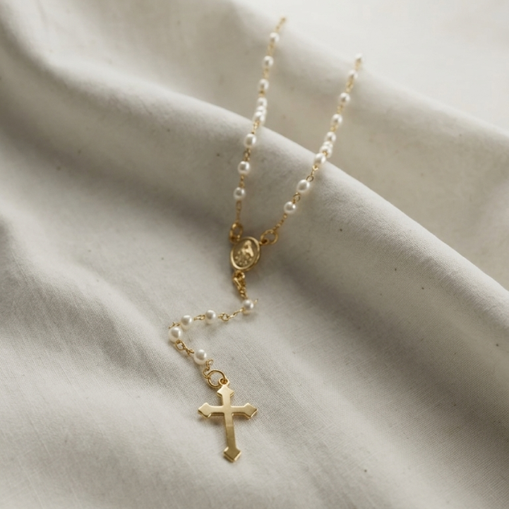 Gold filled pearl cross rosary necklace on a beige fabric background