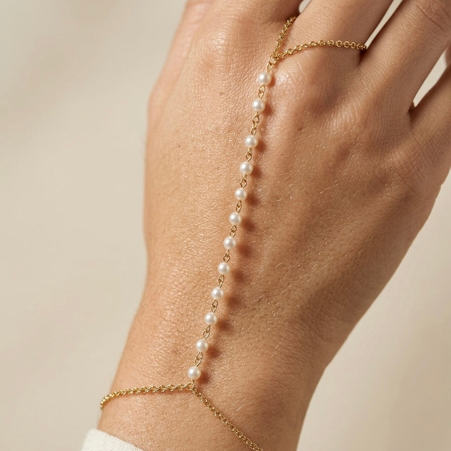Gold hand chain bracelet with pearls on a hand against a neutral background