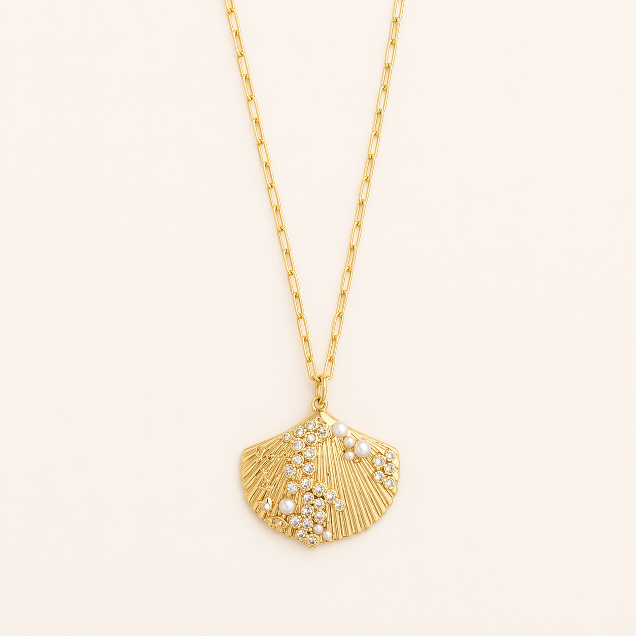 Gold necklace with a shell pendant pearl and crystal accents on a light beige background