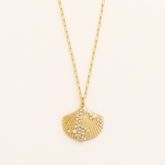 Gold necklace with a shell pendant pearl and crystal accents on a light beige background