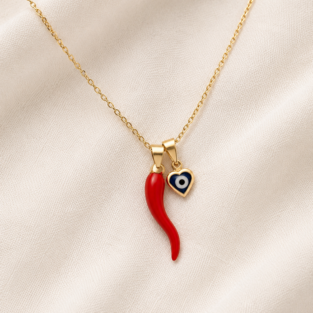 Gold filled necklace with a red italian horn and blue evil eye pendants on a beige fabric background