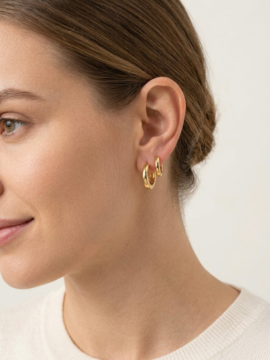 A close-up side profile of a woman wearing a set of gold filled huggie hoop earrings, plain staple design 