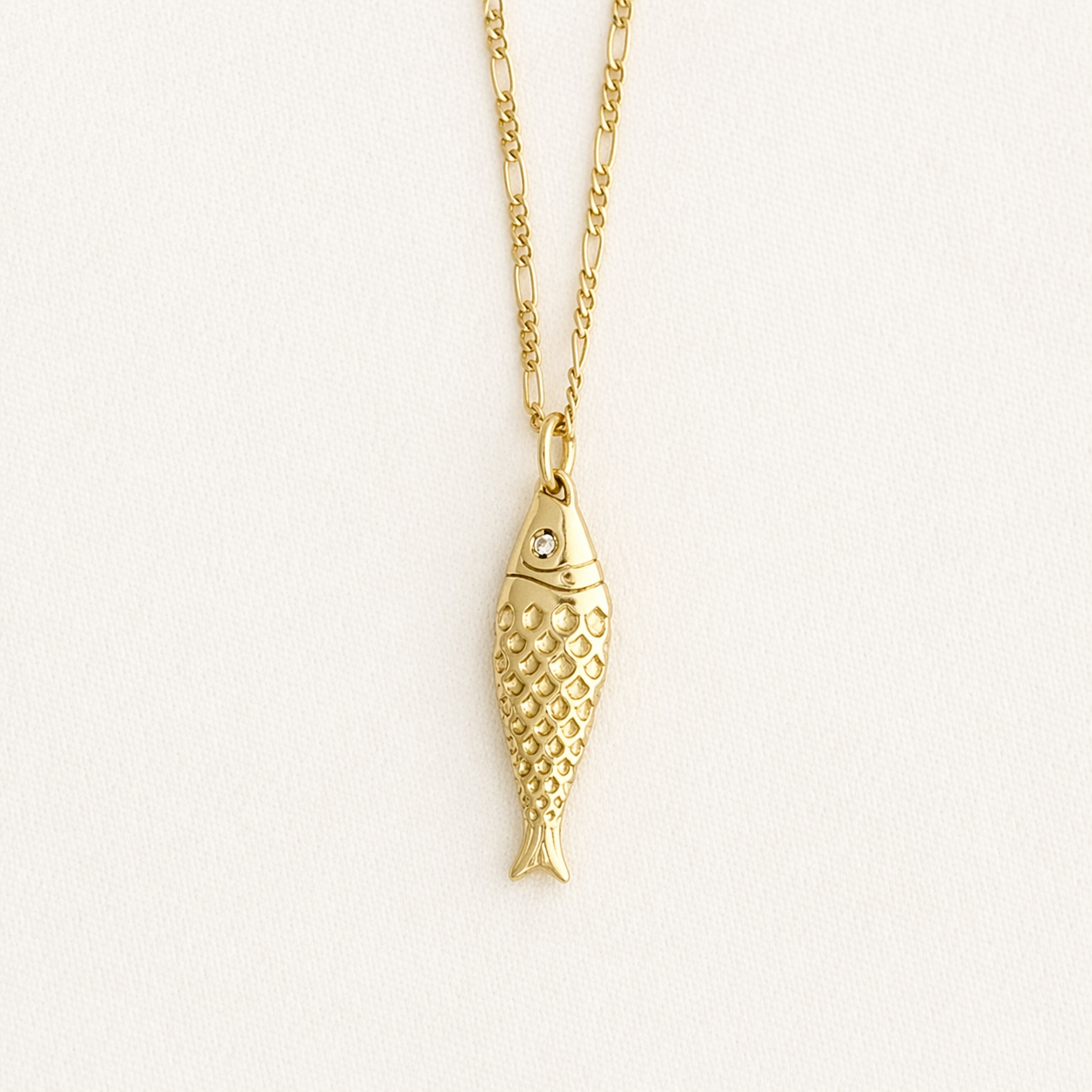 Gold fish-shaped pendant necklace on a light beige background