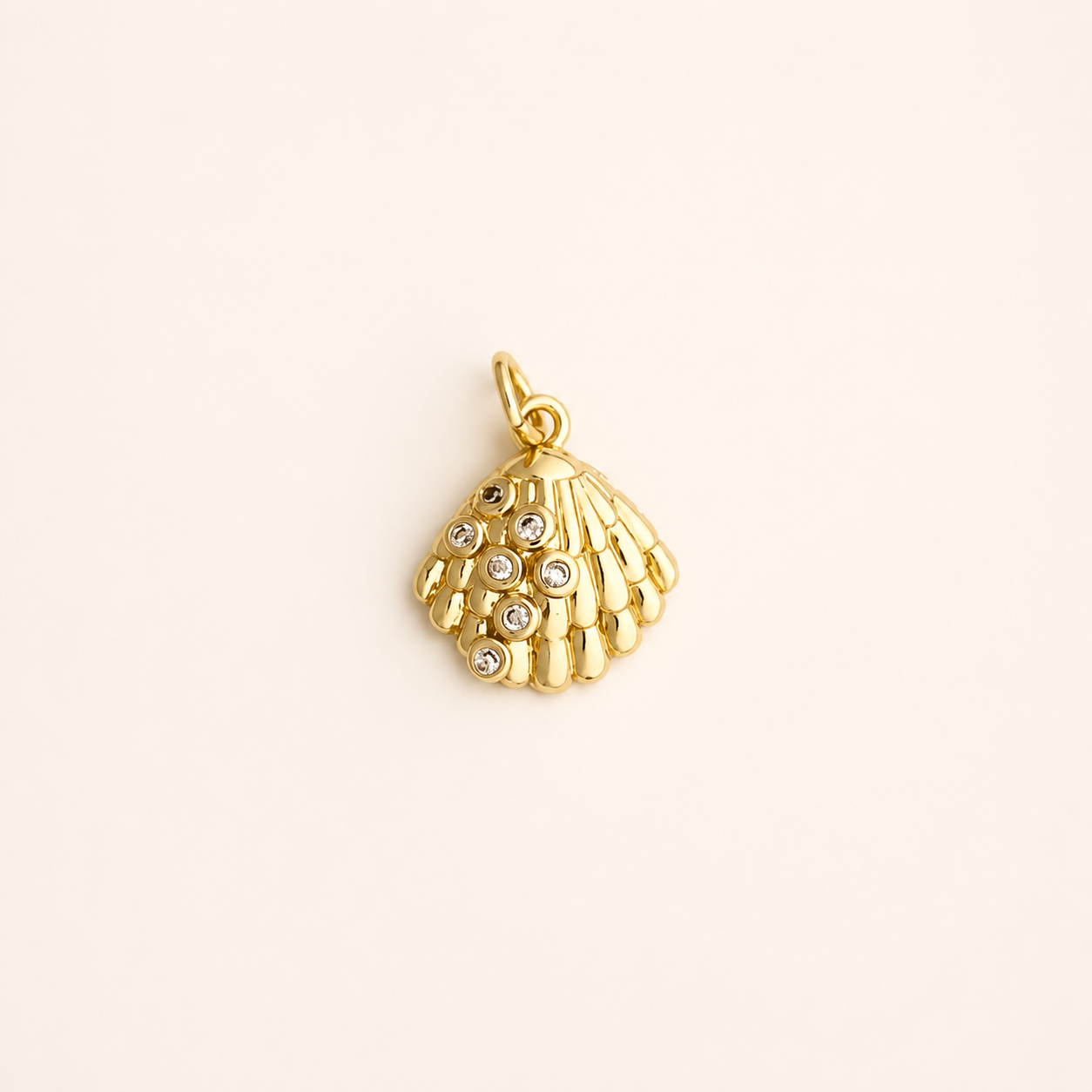 Gold shell pendant with embedded stones on a beige background