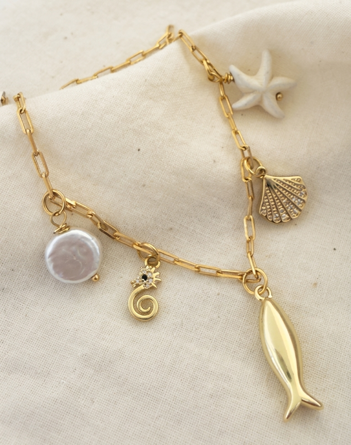 Multicharm necklace over cream linen fabric, necklace is gold filled with fish, seahorse, shell, starfish and pearl charm.