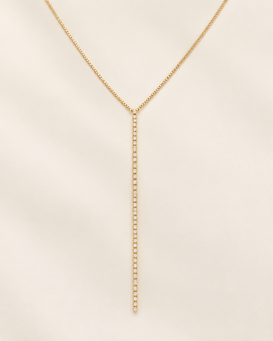 A delicate gold Y-necklace with a long, thin drop chain, displayed on a soft beige fabric background.