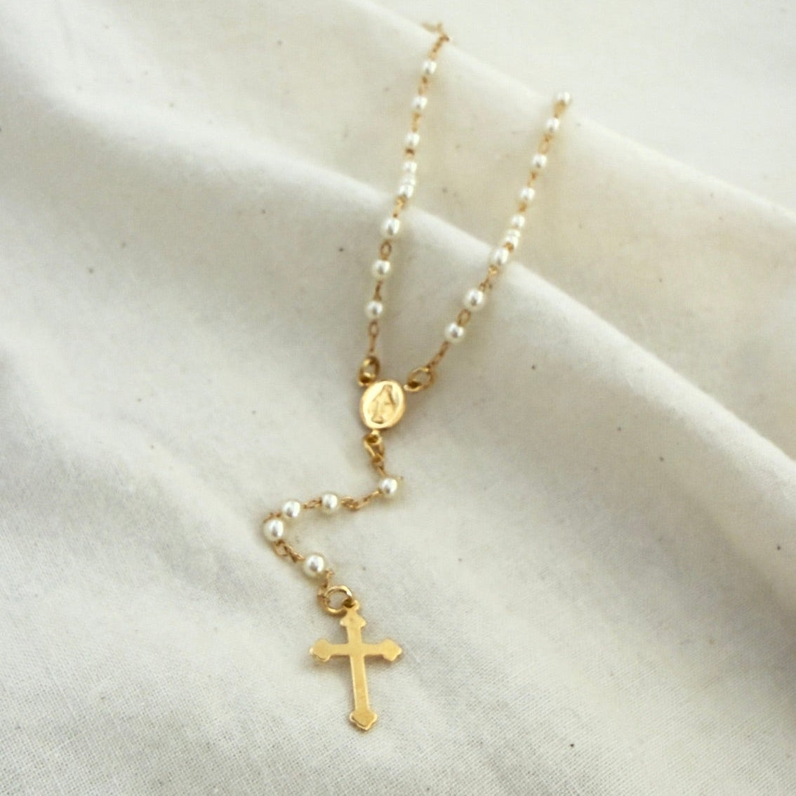 Gold Rosary necklace with cross pendant on a white fabric background