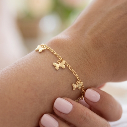 Gold bracelet with butterfly charms on a wrist against a blurred background