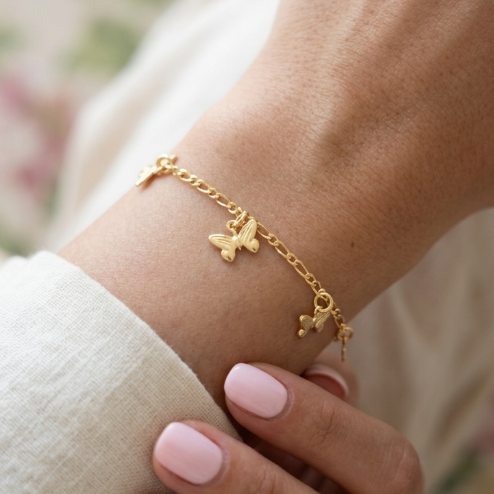 Gold bracelet with butterfly charms on a wrist against a blurred floral background