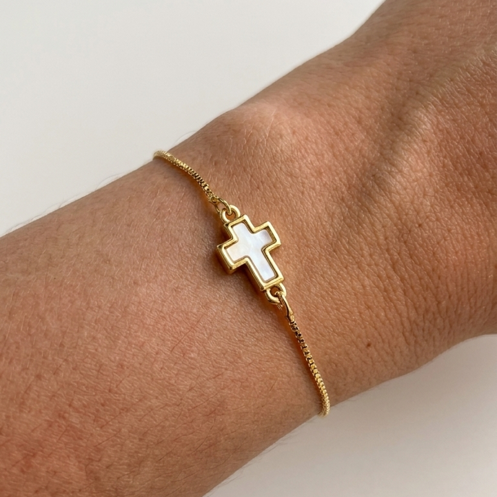 Gold plated adjustable bracelet with a cross charm on a wrist against a white background