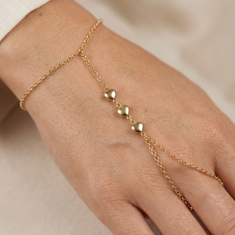 Close up to Gold filled  hand chain with heart-shaped charms on a person's wrist against a neutral background