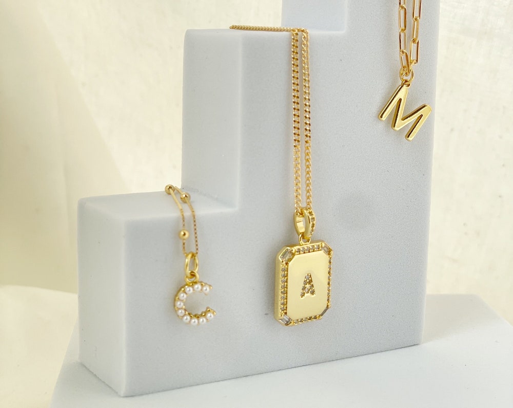 Three styles of Initial necklaces, pearl letter with a satellite necklace. square initial letter with cubic zirconia with a dainty curb chain and gold small plain letter in a 4mm paperclip link necklace. Material 18k gold filled chains, and gold plated charms.  