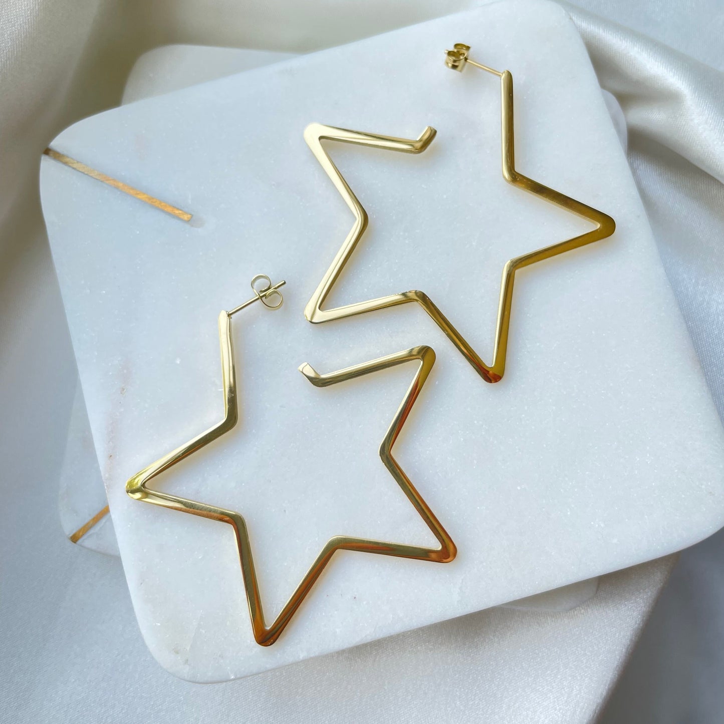 Stainless steel star hoops, 2.5 inches wide, push back hoop earring. Displayed on Marble tray and white silky background