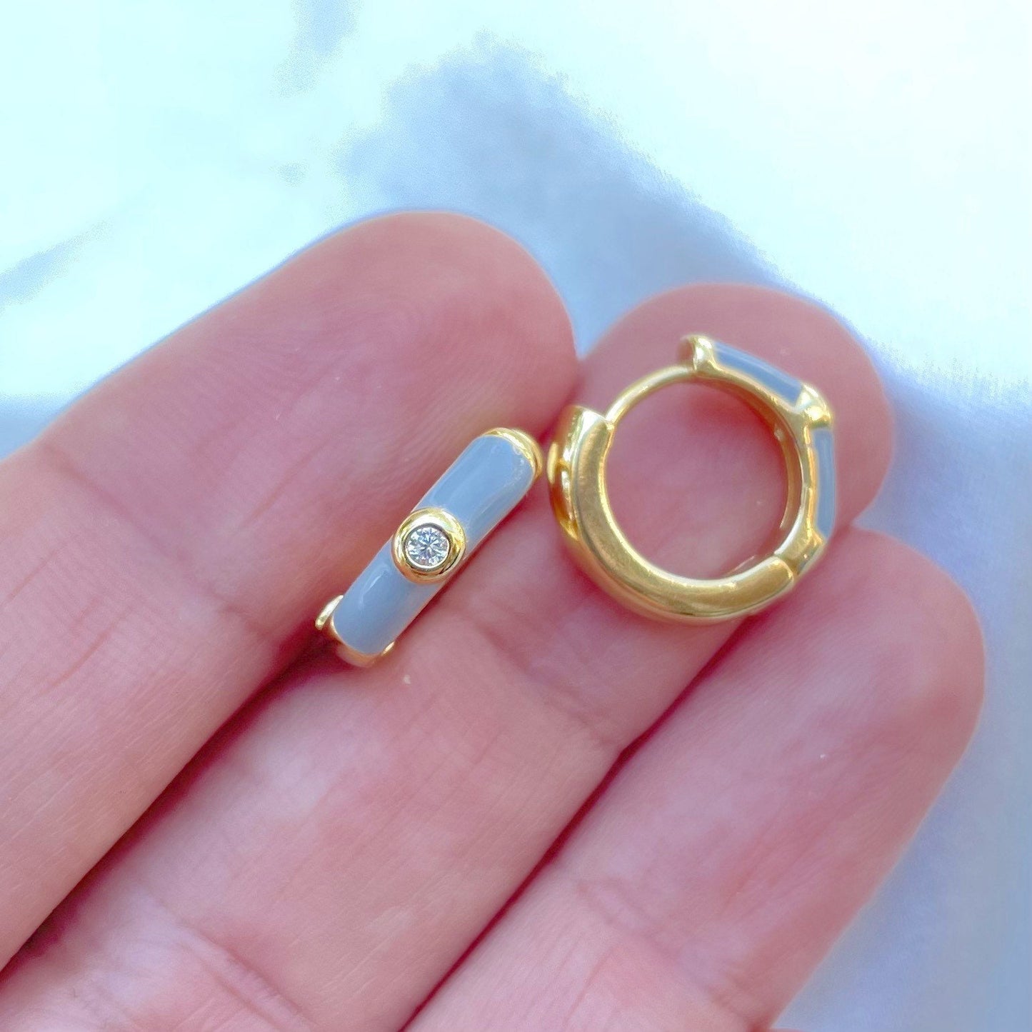 Small grey enamel huggie hoop earring, displayed on hand, material 18k gold filled and a small cubic zirconia