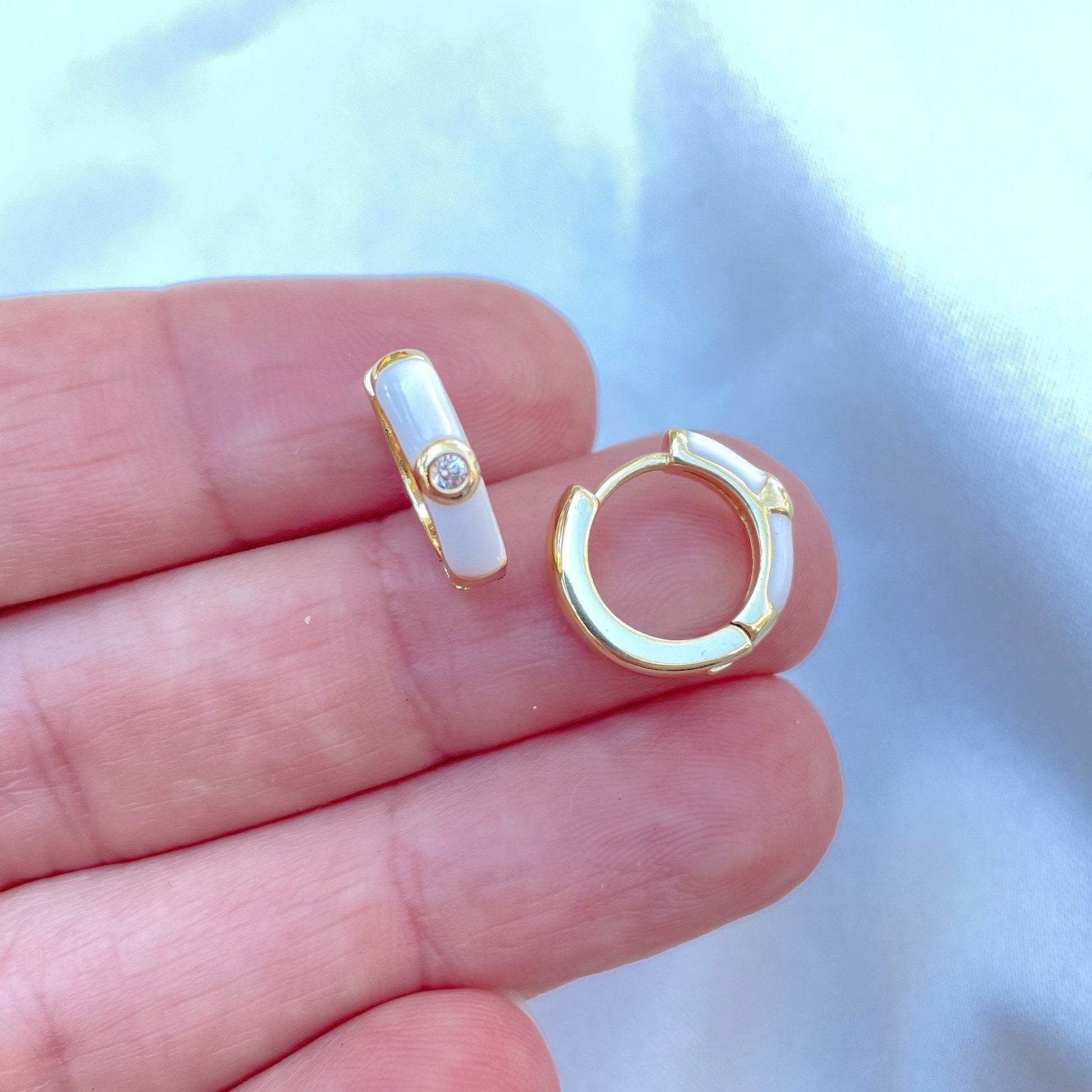 Small white enamel huggie hoop earring, displayed on hand, material 18k gold filled and a small cubic zirconia