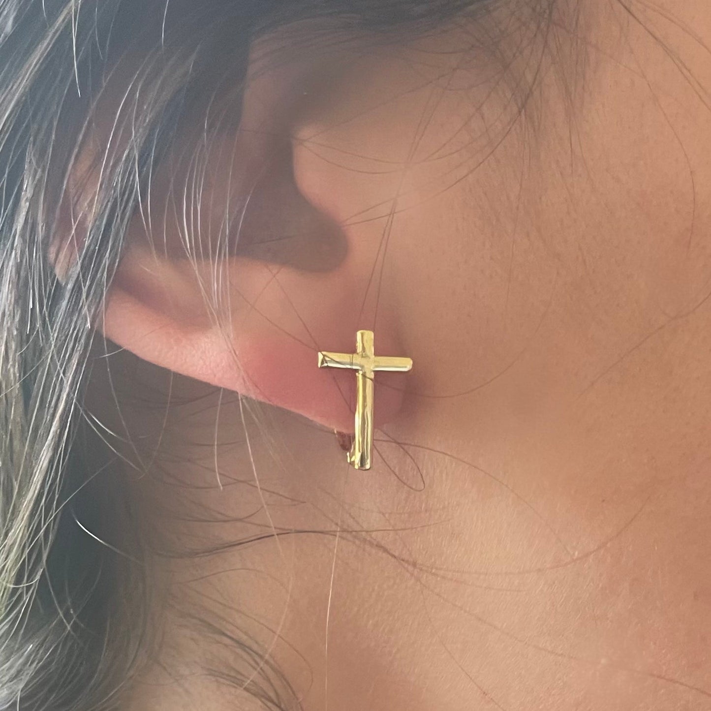 Model wearing gold cross huggie hoop earrings 