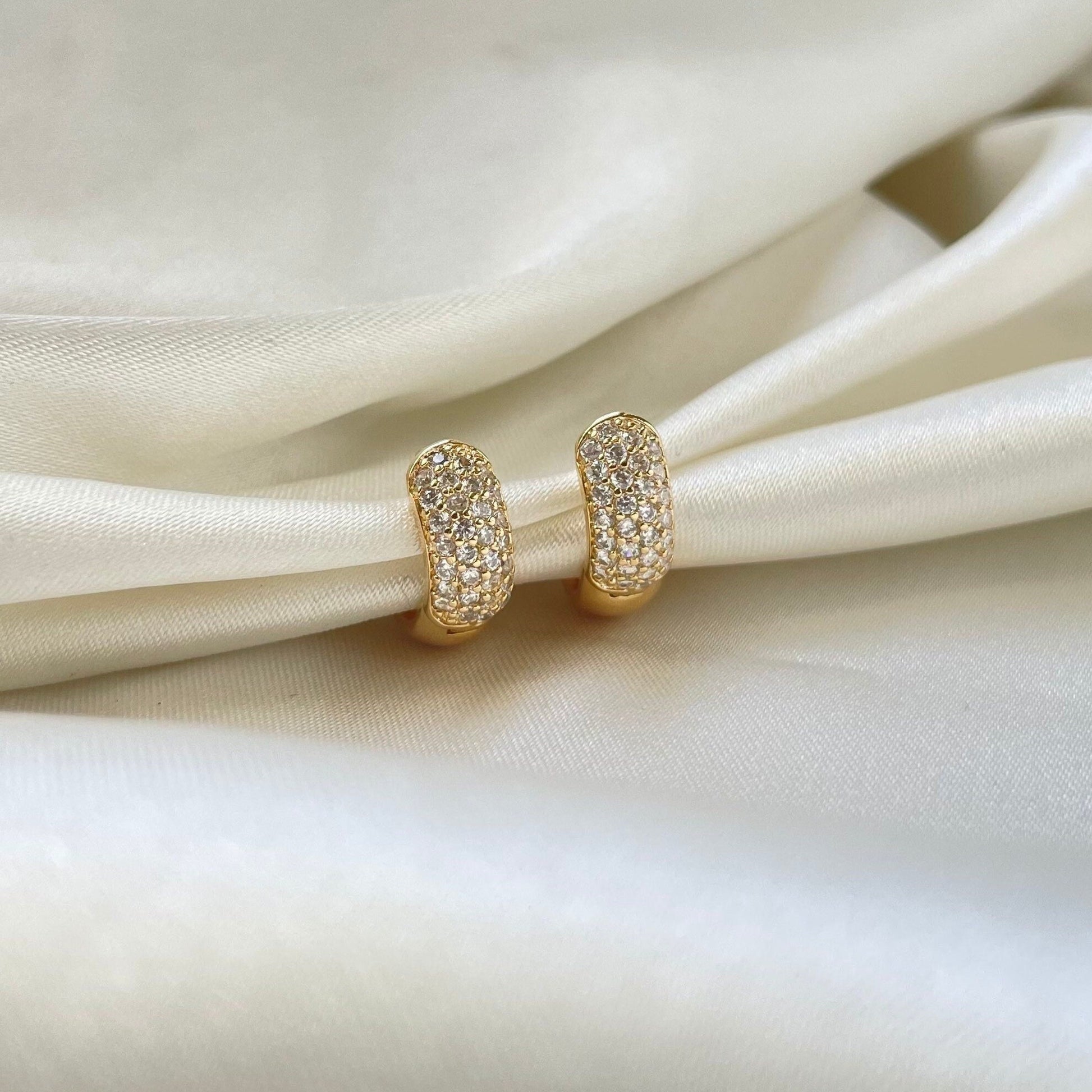 Cz chunky huggie hoop earrings in 18k gold filled. White silky background 