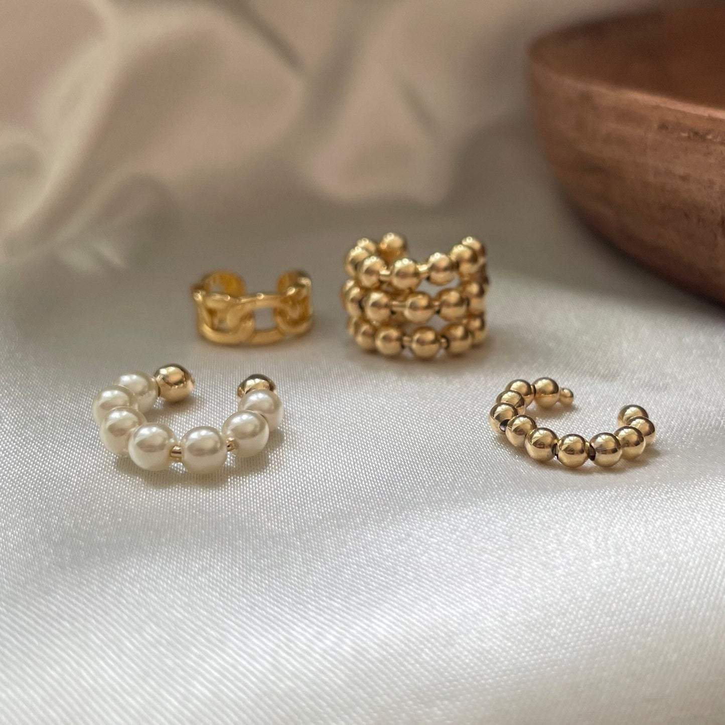 set of 4 ear cuffs: beaded faux pearl ear cuff, beaded simple gold ear cuff, triple beaded gold ear cuff, curb chain style er cuff, all in 18k gold filled. White background and wood tray decor 