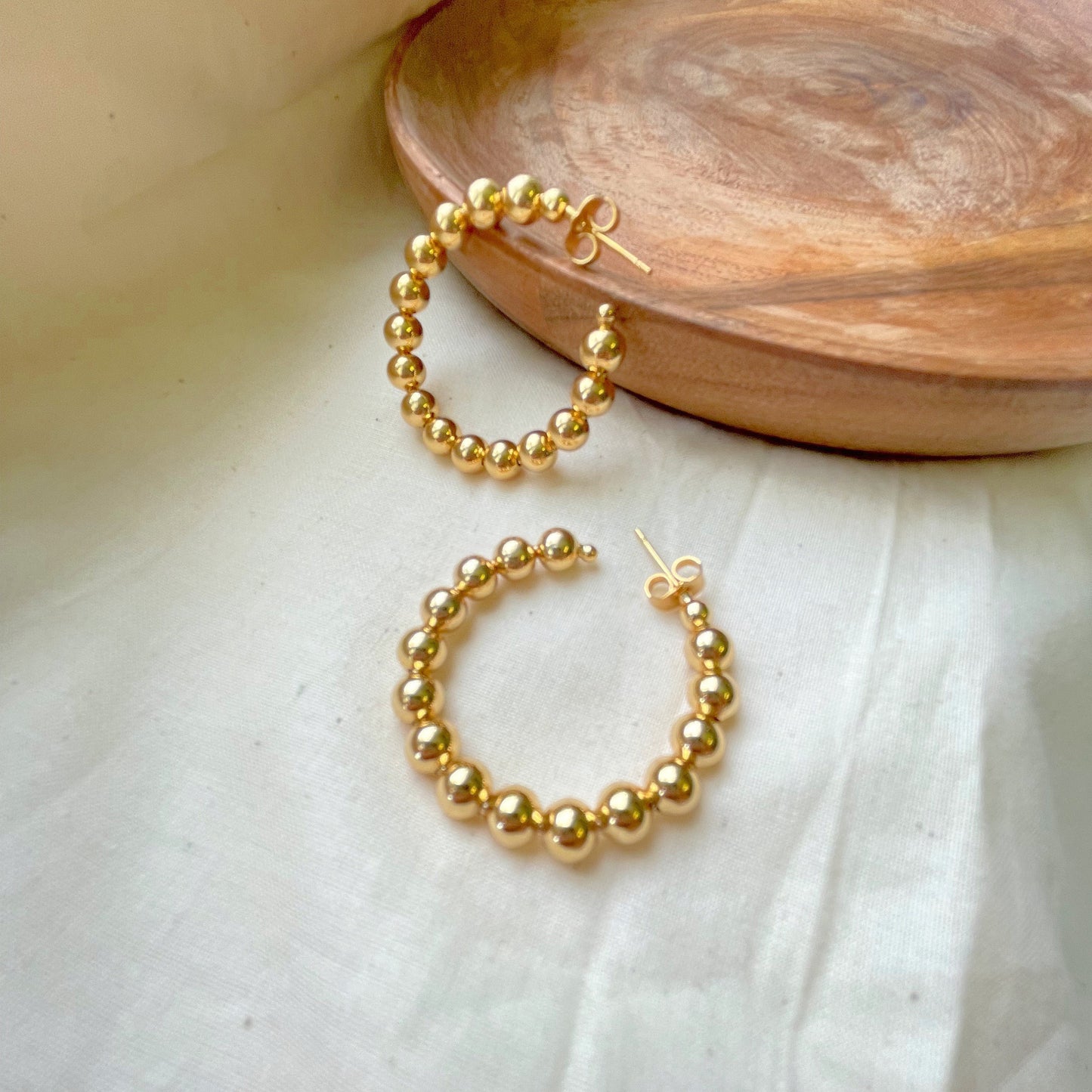 Close look to 1,7 inches wide beaded hoop earring, made of 18k gold filled, open hoop earring closure push back. White silk and wood tray as decor background