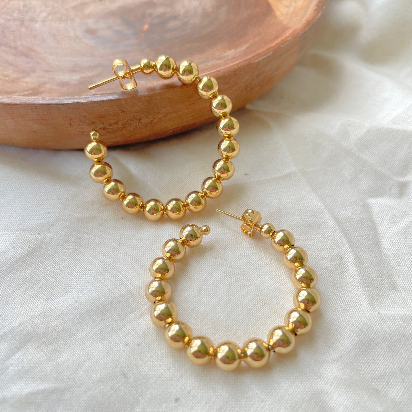 Closer look to 1,7 inches wide beaded hoop earring, made of 18k gold filled, open hoop earring closure push back. White silk and wood tray as decor background