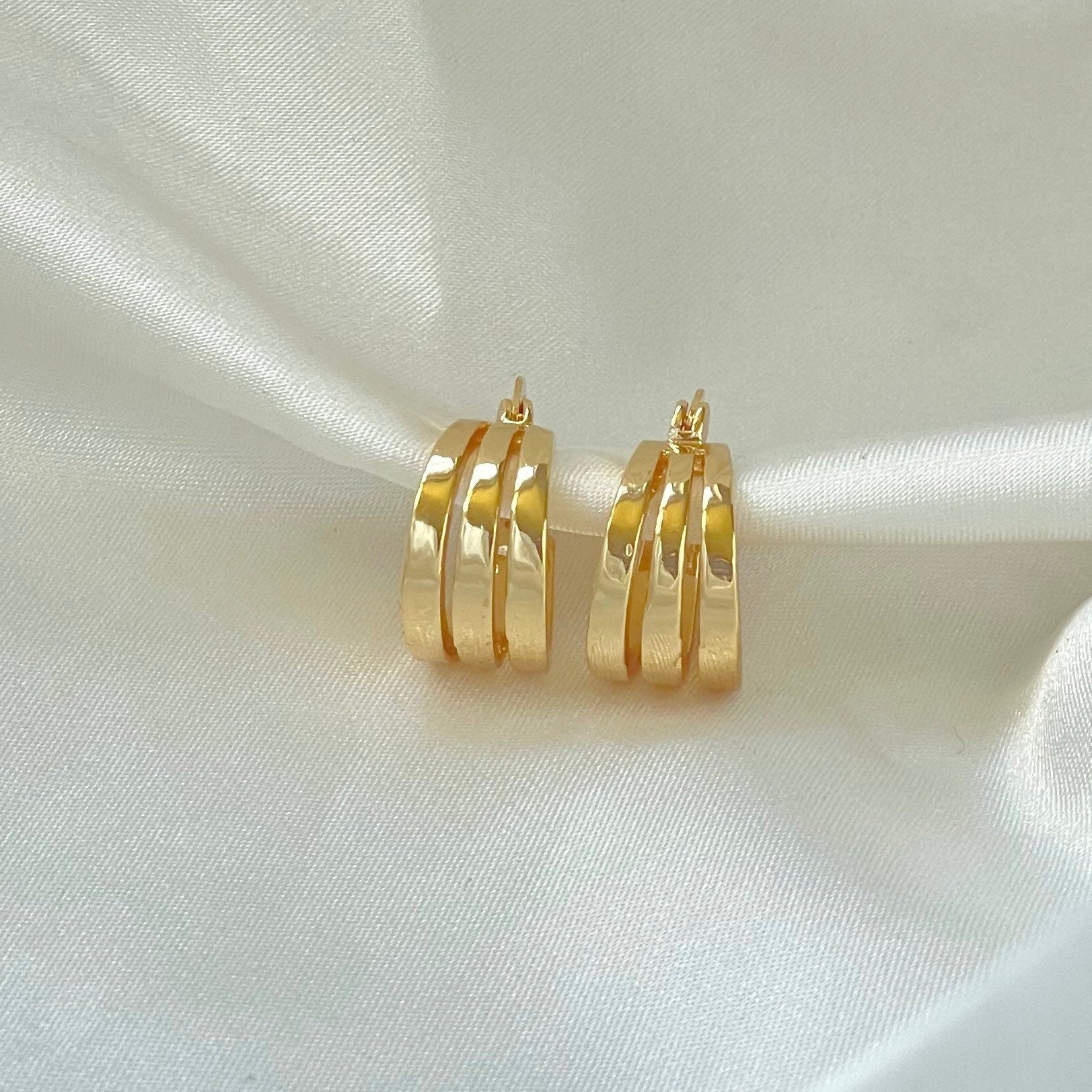 Front view Triple hoop earrings made in 18k gold filled, latch back hoop displayed on white silky fabric. 