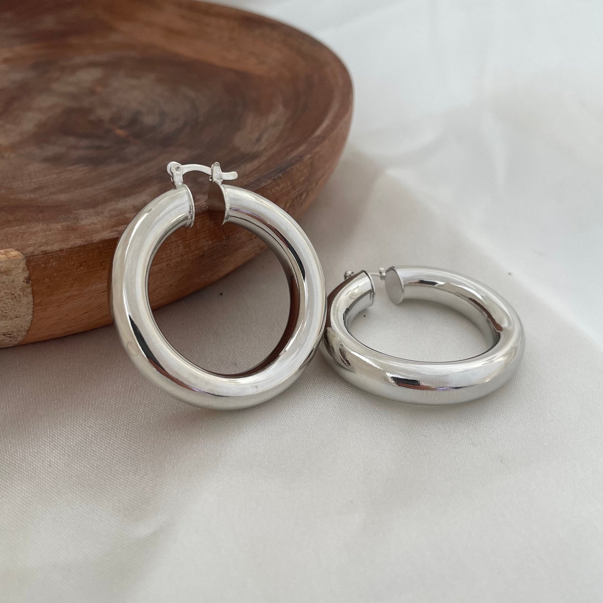 Chunky rhodium filled hoop earrings, 6 mm thick and 1.7 inches diameter. Latch back closure. White silk background and wood tray as decor