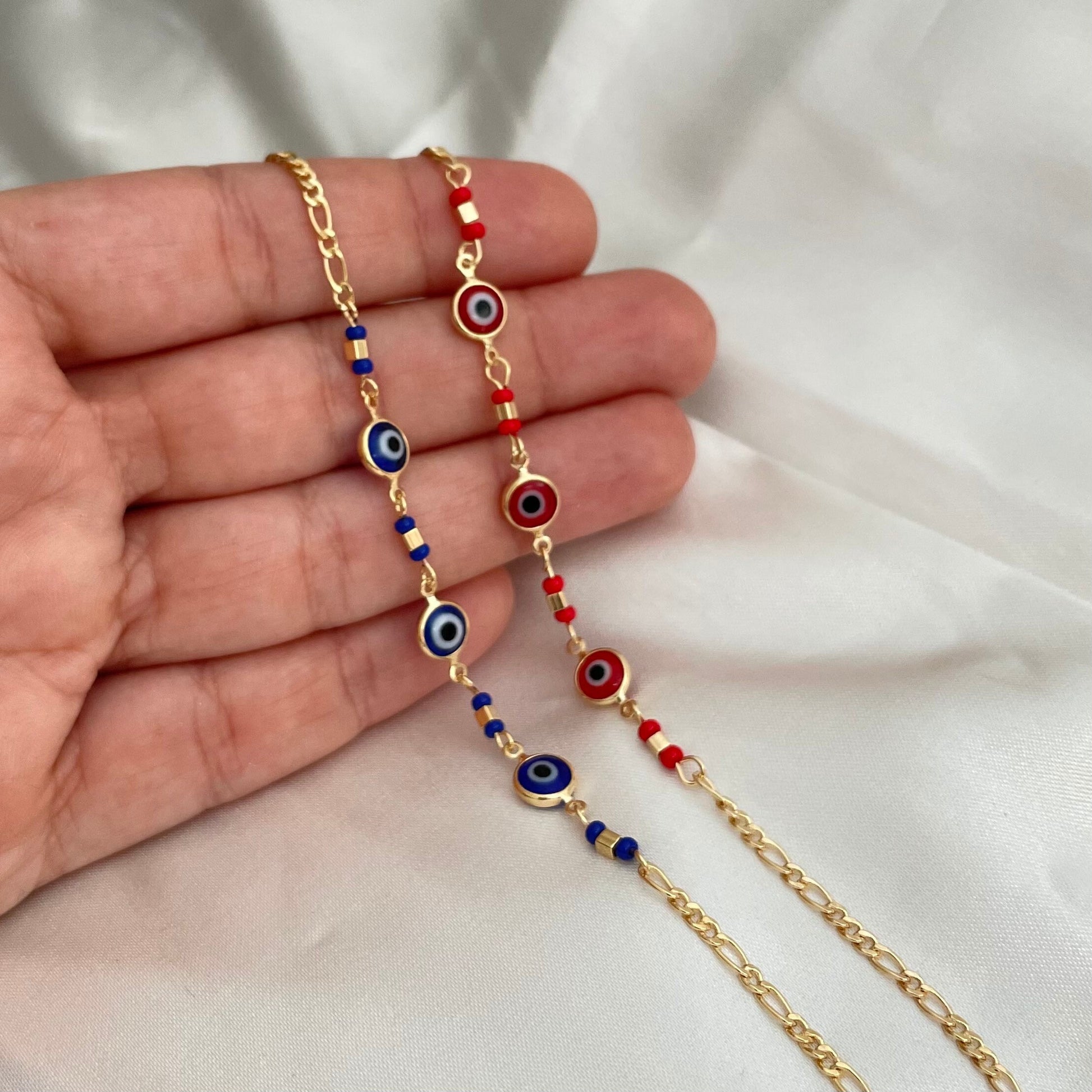 Royal blue and red evil eye bracelets made of 18k gold filled and hold on hand by model. White background 