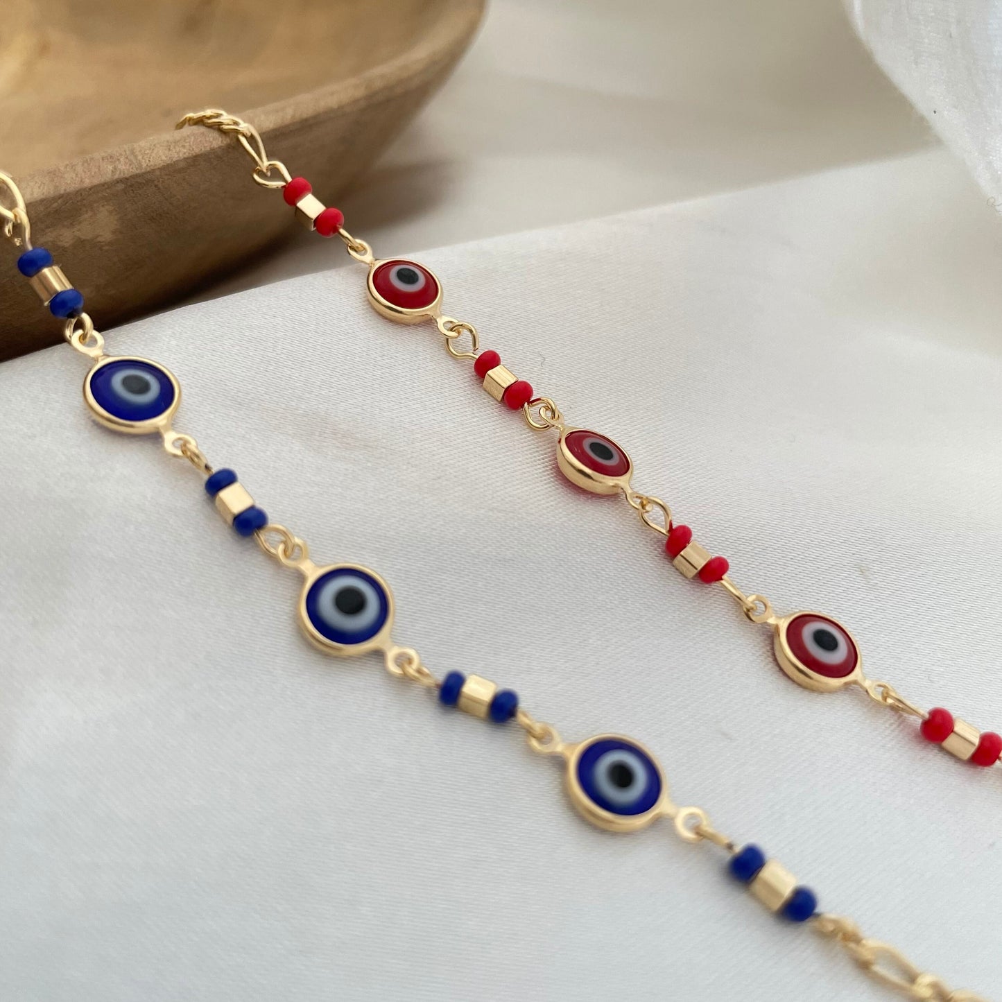 Royal blue and red evil eye bracelets made of 18k gold filled displayed on White silk background 