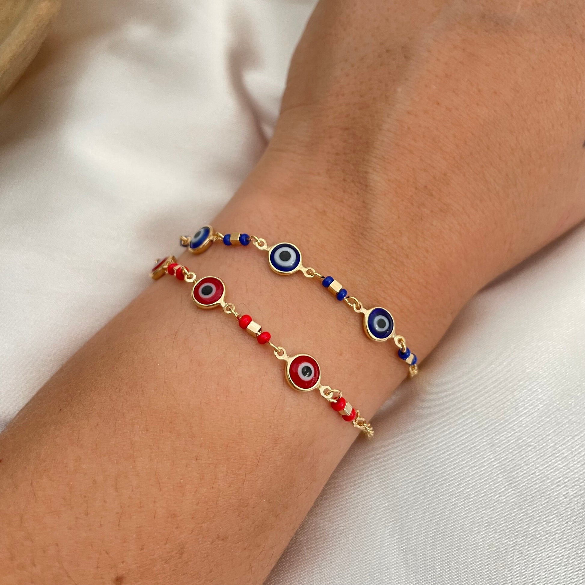 Royal blue and red evil eye bracelets made of 18k gold filled and wore on wrist by model. White background 