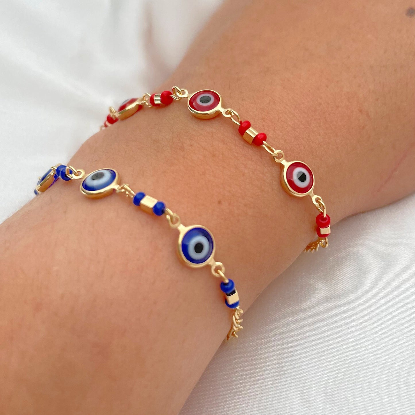 Royal blue and red evil eye bracelets made of 18k gold filled and wore on wrist by model. White background 