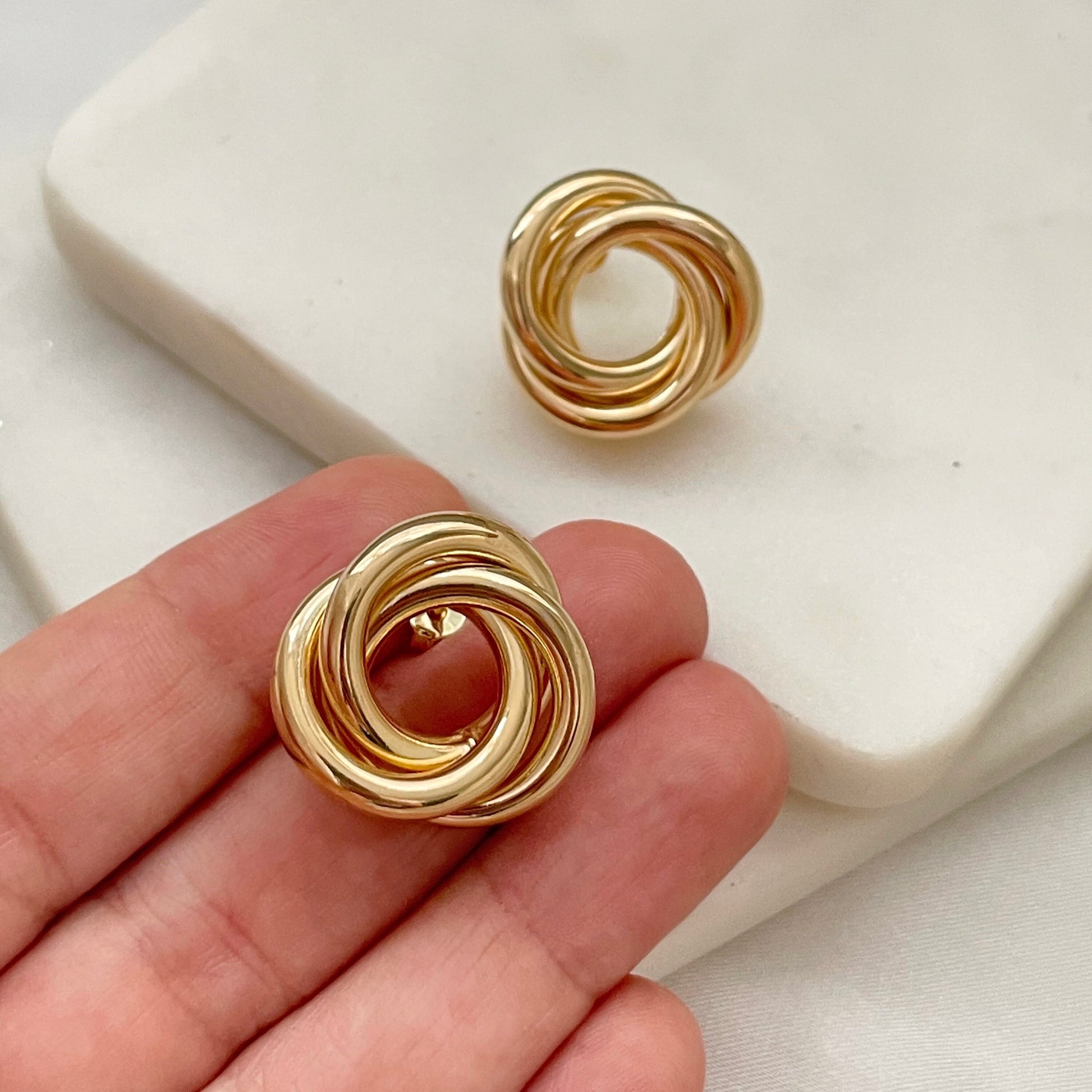 18k gold filled knot stud earrings, chunky and chubby knot earrings displayed on marble and white silk background. Hold on hand by model. 