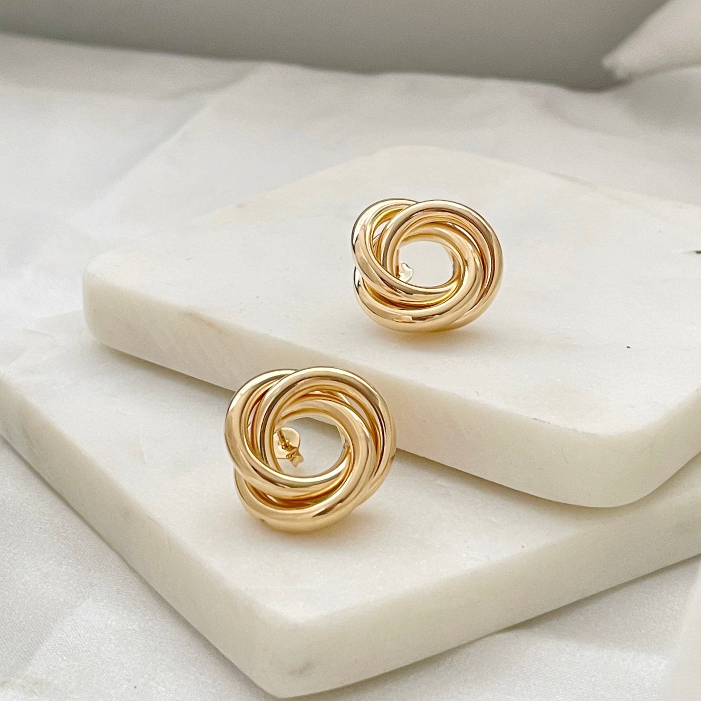 18k gold filled knot stud earrings, chunky and chubby knot earrings displayed on marble and white silk background 