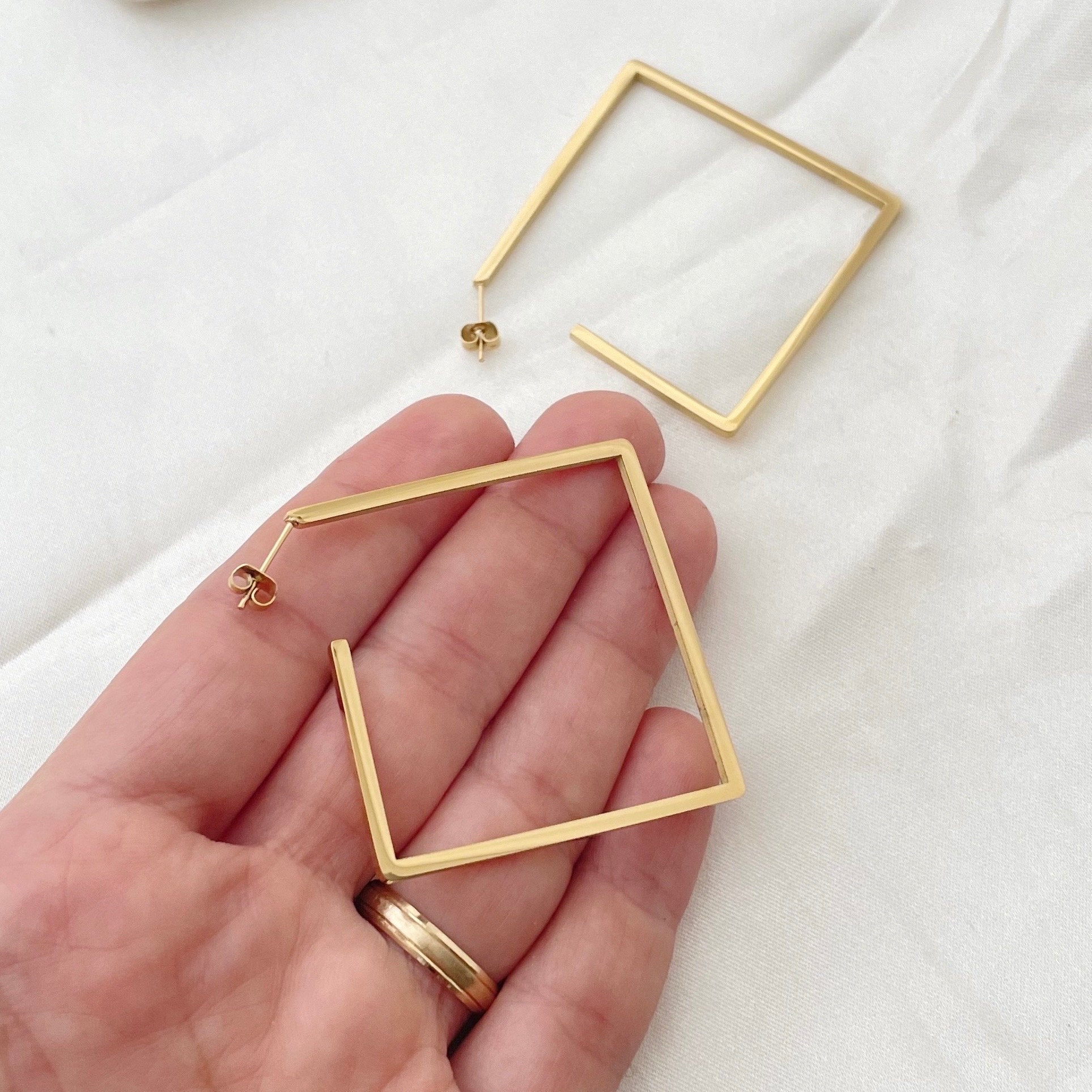 Stainless steel square hoops, 2.5 inches wide, push back hoop earring. Shown on hand to appreciate size. White silky background