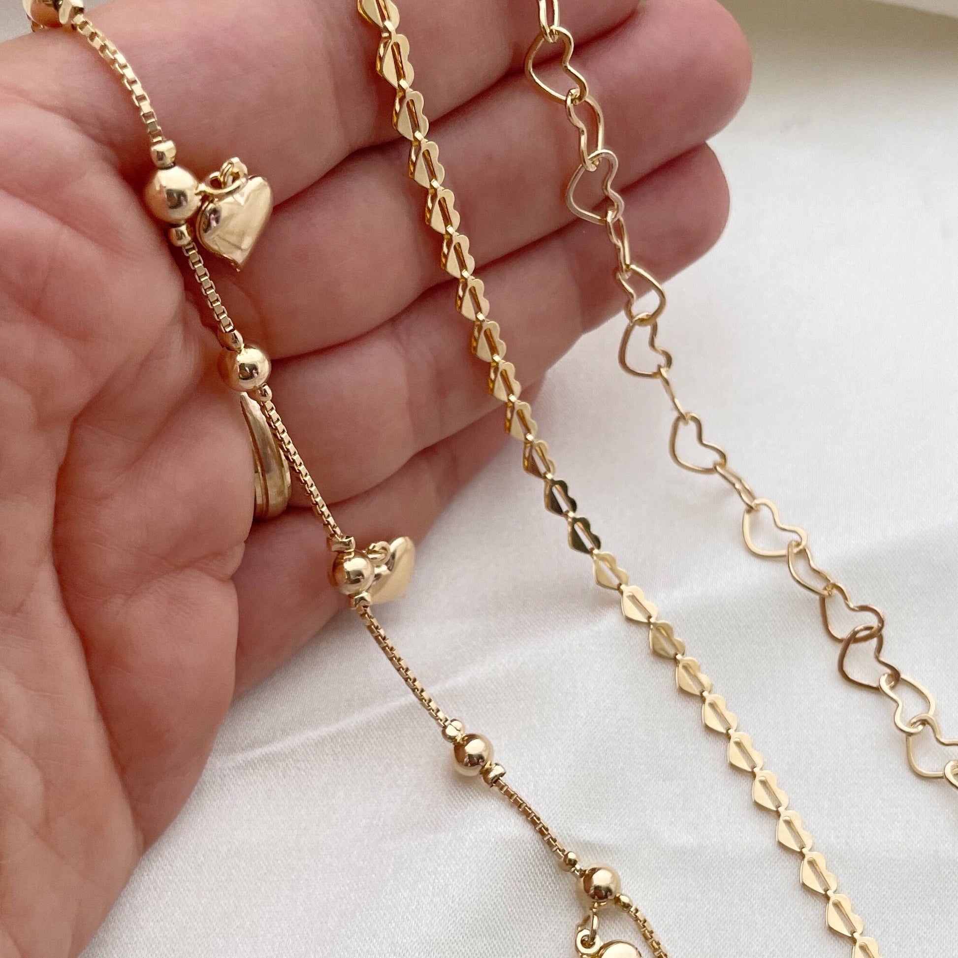 Set of 3 18k gold filled heart bracelets, 3 different styles: full heart bracelet, hollow heart link chain and dangle heart  bracelets. These are being shown with detail on hand 