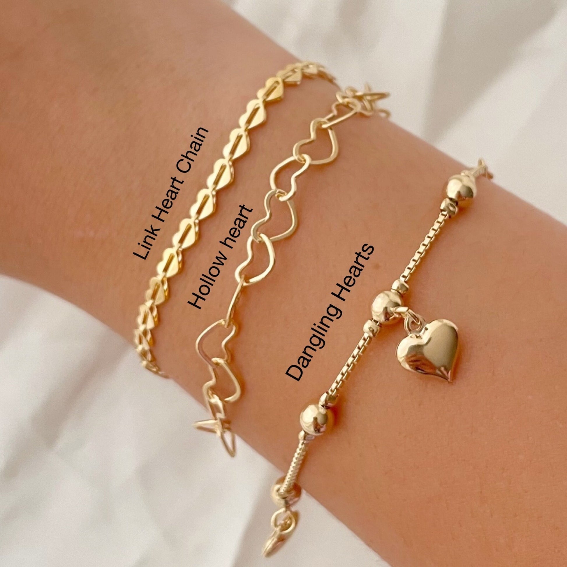 Set of 3 18k gold filled heart bracelets, 3 different styles: full heart bracelet, hollow heart link chain and dangle heart  bracelets. Displayed on arm. Description added to each bracelet 