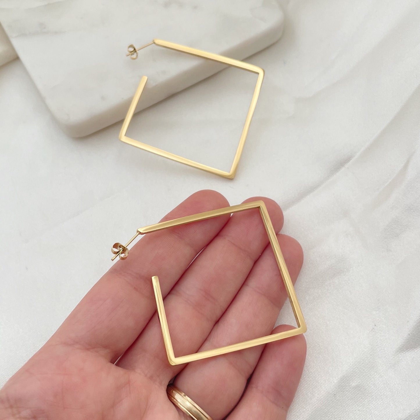 Stainless steel square hoops, 2.5 inches wide, push back hoop earring. Shown on hand to appreciate size. Marble tray and white silky background