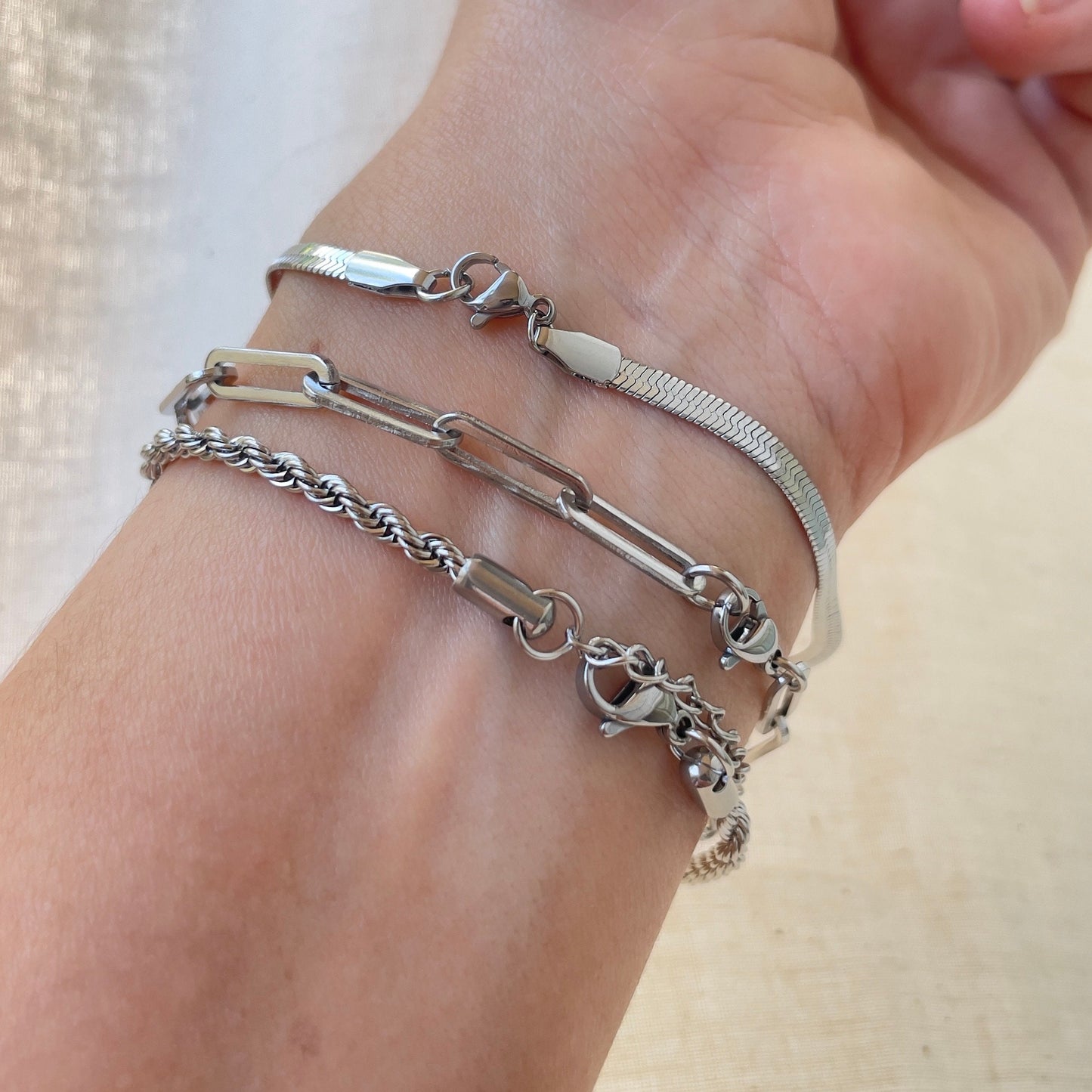 3 stainless steel bracelets displayed on wrist. Thick paperclip bracelet, 4mm herringbone and 4 mm rope bracelet shown lobster close. 