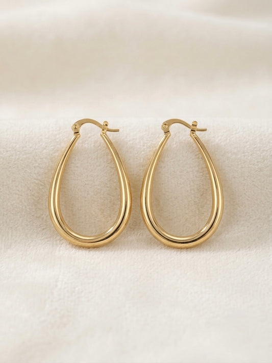 A pair of gold filled teardrop hoop earrings with a polished finish, displayed on a soft, textured cream fabric background.